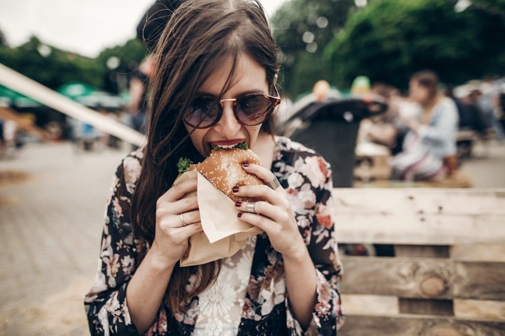 The Best Food Festivals in Quebec in 2025 Boho girl biting cheeseburger, smiling at street food festival