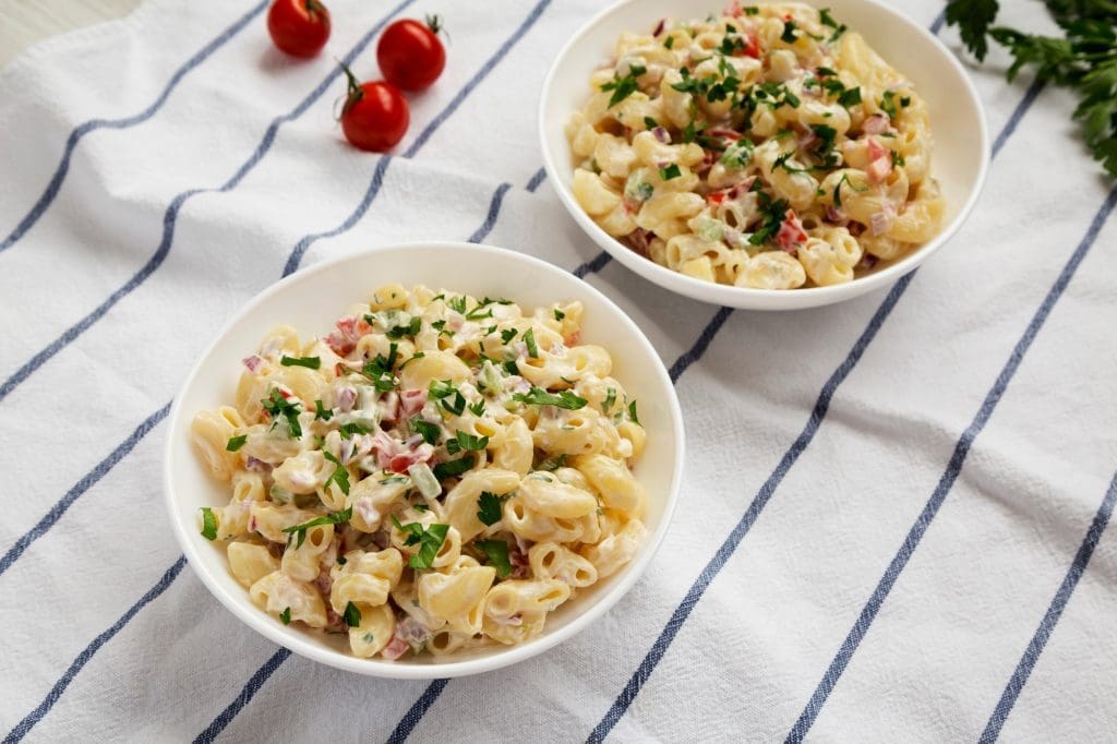10 Recettes de Salades Savoureuses pour Toutes les Occasions Homemade Macaroni Salad in white bowls, low angle view.