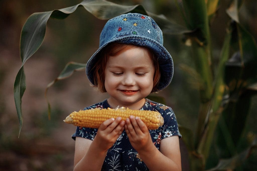 Blé d’Inde : les méthodes pour savourer ce classique Happy little girl holding an ear of corn.